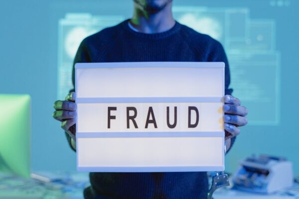 A man holding a sign reading 'FRAUD' in a tech environment, highlighting cybersecurity concerns.